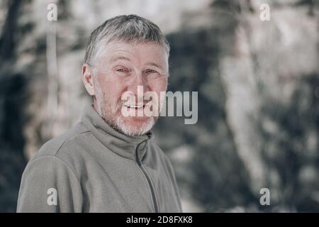 Porträt eines unrasierten attraktiven und glücklichen Mannes mittleren Alters im Freien. Blickt lächelnd in die Kamera. Menschen und Lifestyle-Konzept. Leerzeichen für Text. Stockfoto