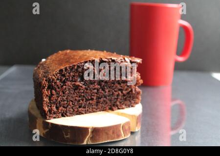 Schokoladenbrownie Pie auf einem Holzständer Blockhütte zurück Im Hintergrund ist ein roter Becher A Cup of Tee Kaffee Milch auf einem schwarzen Hintergrund mit einer Kopie Platz Stockfoto