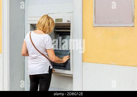 Blonde weiße Frau zieht Bargeld von einem Geldautomaten Stockfoto