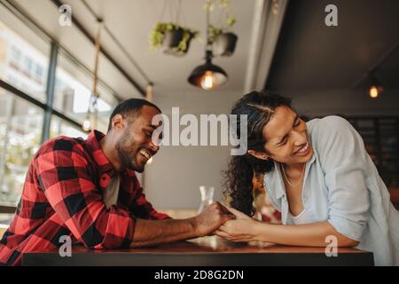 Mann und Frau sitzen im Café und halten sich die Hände und lächeln. Liebevolles Paar genießt auf einem Date im Coffee Shop. Stockfoto