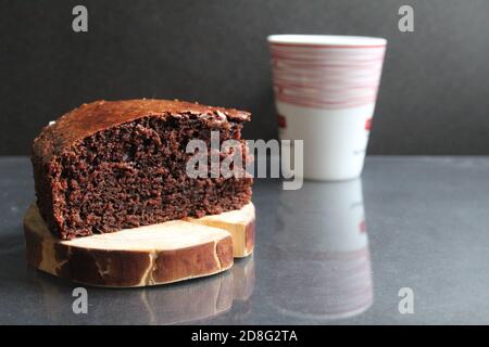 Schokoladenbrownie Pie auf einem Holzständer Blockhütte zurück Im Hintergrund ist ein weißer Becher eine Tasse Tee Kaffee Milch auf einem schwarzen Hintergrund mit einer Kopie Spa Stockfoto