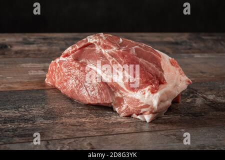 Schweinefleisch. Großes Stück rohes Schweinefleisch auf einem dunklen rustikalen Tisch. Stück fettes Schweinefleisch auf dunkelschwarzem Hintergrund Stockfoto