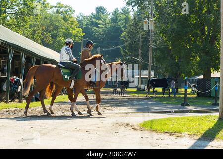 Reiten in einem Stall vor dem Saratoga Pferderennen. Schöne Aufnahme von 2 Personen auf braunhaarigen Pferden im Sonnenlicht. Stockfoto
