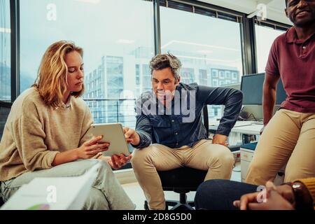 Ein vielfältiges Team von Designern diskutiert über neue Projekte. Kaukasische Männer und Frauen Forschung Ideen auf digitalen Tablet sitzen im Büro Stockfoto