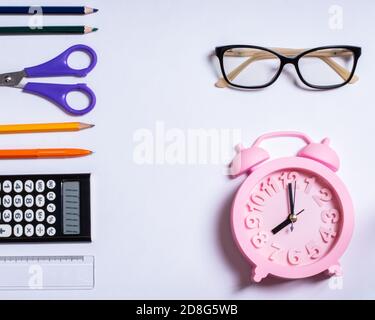 Farbige Schulbedarf, Brille und rosa Wecker auf weißem Hintergrund, Kopierraum, Design Stockfoto