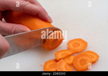 Draufsicht auf Frauenhänden, die rohe Karotten in Runde schneiden Scheiben mit einem Messer auf weißem Hintergrund Stockfoto