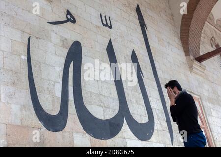 Junger Mann starrte auf die arabische Kalligraphie bedeutet "Allah-Gott in Islam' an der Mauer der alten Edirne Moschee Stockfoto