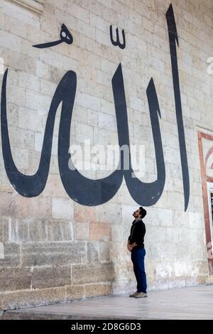 Junger Mann starrte auf die arabische Kalligraphie bedeutet "Allah-Gott in Islam' an der Mauer der alten Edirne Moschee Stockfoto