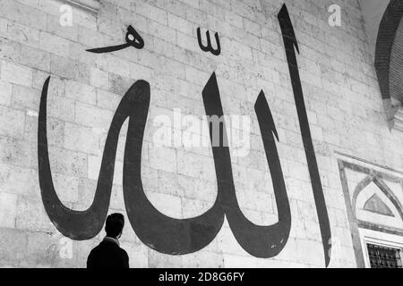 Junger Mann starrte auf die arabische Kalligraphie bedeutet "Allah-Gott in Islam' an der Mauer der alten Edirne Moschee Stockfoto