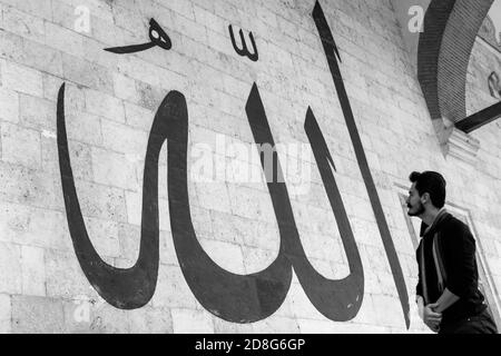 Junger Mann starrte auf die arabische Kalligraphie bedeutet "Allah-Gott in Islam' an der Mauer der alten Edirne Moschee Stockfoto