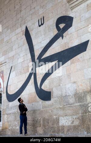 Junger Mann starrt auf die arabische Kalligraphie und bedeutet 'Prophet Muhammad' An der Mauer der alten Edirne Moschee Stockfoto