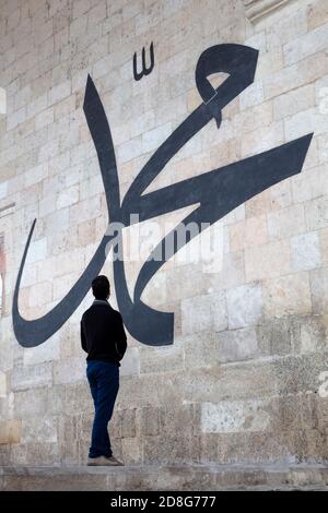 Junger Mann starrt auf die arabische Kalligraphie und bedeutet 'Prophet Muhammad' An der Mauer der alten Edirne Moschee Stockfoto