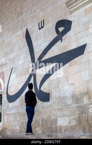 Junger Mann starrt auf die arabische Kalligraphie und bedeutet 'Prophet Muhammad' An der Mauer der alten Edirne Moschee Stockfoto