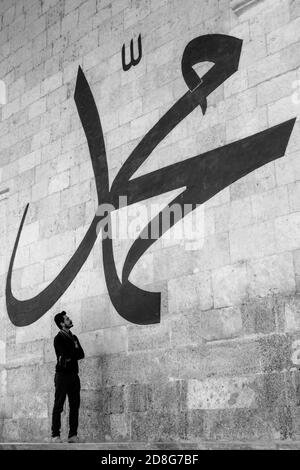 Junger Mann starrt auf die arabische Kalligraphie und bedeutet 'Prophet Muhammad' An der Mauer der alten Edirne Moschee Stockfoto