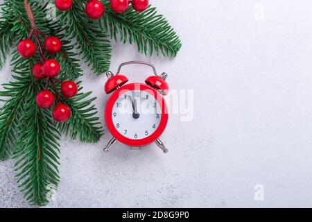 Weihnachtskomposition mit rotem Wecker, Tannenzweigen und Stechpalme auf Steingrund. Neujahrskonzept. Draufsicht. Kopierbereich - Bild Stockfoto