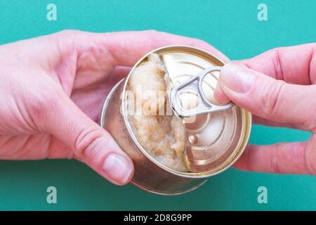 Die Hand eines erwachsenen Mannes hält eine Dose Konserven, die zweite Hand öffnet den Deckel und ruckert einen Schlüssel Stockfoto