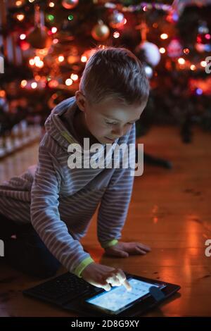 Sieben Jahre alter Junge mit Tablet und Christamsbaum in Der Hintergrund Stockfoto