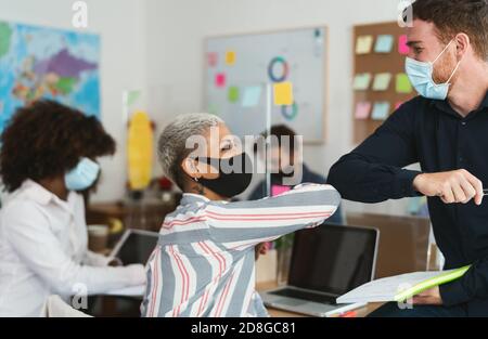Junge multirassische Arbeiter tragen Gesichtsmaske tun neue soziale Distanz Grüße stoßen Ellbogen im Co-Working kreativen Raum Stockfoto
