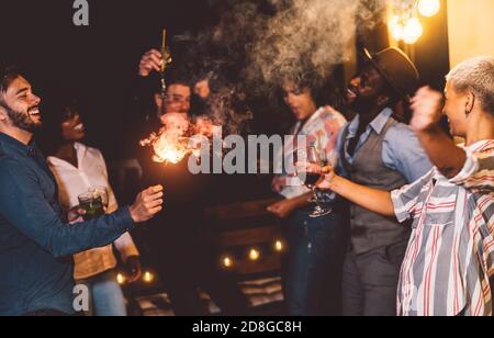 Glückliche junge Freunde tanzen und feiern Silvester mit Wunderkerzen Feuerwerk während Cocktails auf Terrasse House Party trinken Stockfoto