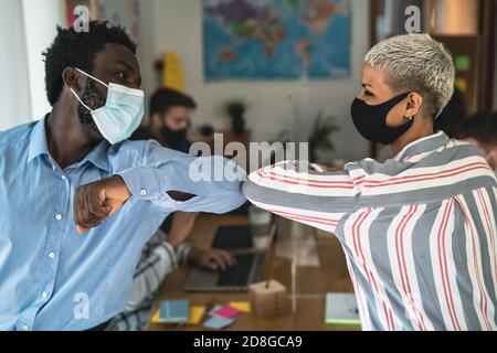 Junge multirassische Arbeiter tragen Gesichtsmaske tun neue soziale Distanz Grüße stoßen Ellbogen im Co-Working kreativen Raum Stockfoto
