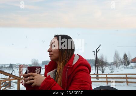 Frau trinkt heißen Tee oder Kaffee aus Festliche Tasse mit verschneiten Berg Blick auf den Hintergrund. Schönes Mädchen genießen Winter Morgen oder Abend im Freien Stockfoto