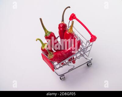 Rote Chilischoten in einem Korb auf Rädern. Rote Paprika auf weißem Hintergrund Stockfoto
