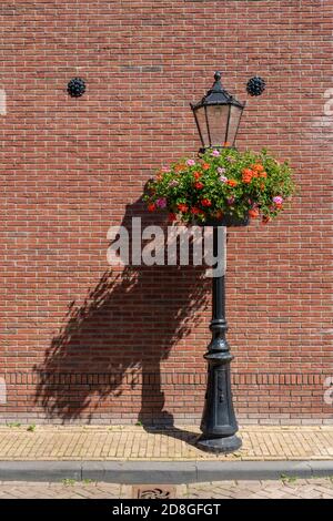 Retro Vintage Lampe und Laterne ist aus Gusseisen. Historische Beleuchtung auf der Straße bei sonnigem Tageslicht, Backsteinmauer im Hintergrund. Stockfoto