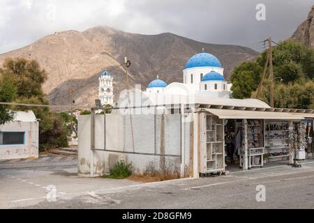 Perissa, Santorini Island, Griechenland - 19. September 2020: Blick auf die blauen Kuppeln Heiliger Kreuz Perissa. Shop mit Souvenirs vor. Stockfoto