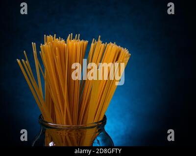 Gelbe Spaghetti Makkaroni steht in einem Glas auf dunklem Hintergrund. Leer für Designer Stockfoto