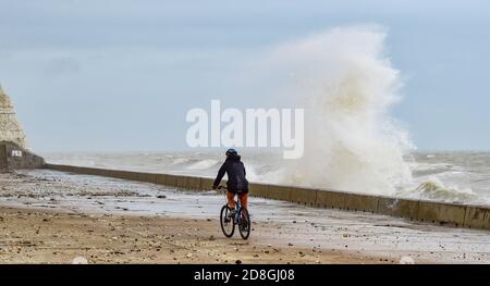 Brighton UK 30. Oktober 2020 - EIN Radfahrer passiert an diesem Morgen Wellen, die über den undercliff Walk in Saltdean in der Nähe von Brighton krachen. Warnungen wurden veröffentlicht, dass stürmisches Wetter für viele Teile des Vereinigten Königreichs am kommenden Wochenende prognostiziert wird : Credit Simon Dack / Alamy Live News Stockfoto