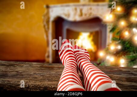 Wollsocken und Frauenbeine auf Holztisch. Platz für Dekoration. Kamin in der häuslichen Innenausstattung mit warmen orangefarbenen Licht des Feuers.Copy Raum Stockfoto