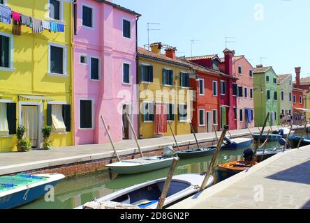 Ein Blick vom Bürgersteig auf einen typischen Kanal auf der Insel Burano, Venedig, mit einigen angedockten Booten und typischen bunten Häusern Stockfoto