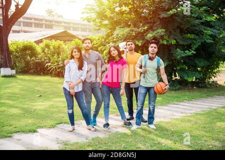 Fröhliche indische asiatische junge Gruppe von Studenten oder Freunden lachen zusammen, während sitzen, stehen oder gehen auf dem Campus Stockfoto