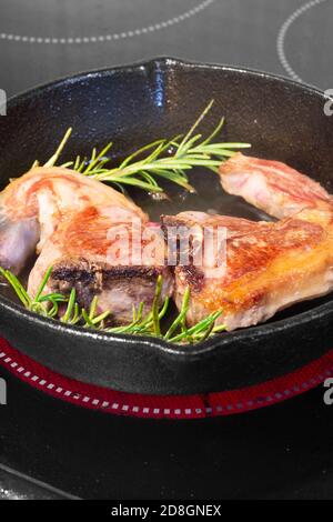 Lammkoteletts mit Rosmarin in einer gusseisernen Pfanne. Kochen auf einem Elektroherd Stockfoto