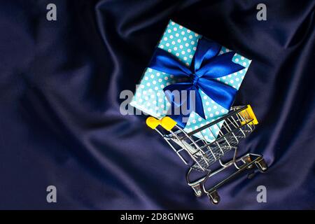 Warenkorb mit blauer Geschenkbox mit Schleife auf blauem Hintergrund. Weihnachtskarte. Stockfoto