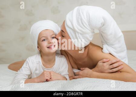 Mutter und ihre Tochter spielen und umarmen im Bett. Kleines Mädchen mit Mama im Handtuch. Glückliche liebevolle Familie. Schöne junge Frau von einem Cu geküsst Stockfoto