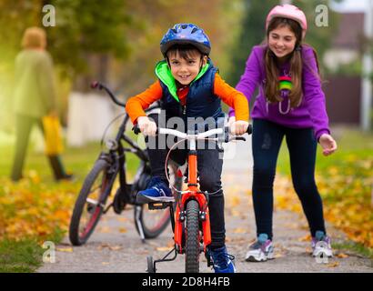 Herbsttag. Schwester lehrt ihren kleinen Bruder Fahrrad zu fahren und freut sich über seinen Erfolg. Familie und gesunder Lebensstil Stockfoto