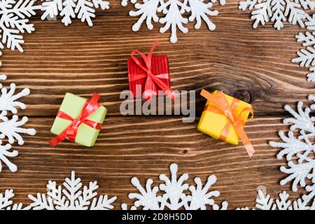 Draufsicht auf kleine Geschenkschachteln in der Nähe von dekorativen Schneeflocken auf Holzhintergrund, Neujahr-Konzept Stockfoto