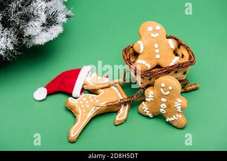 Lebkuchenmänner und Hirsche in santa hat in der Nähe dekorative Schlitten, und Tannenzweig mit Schnee auf grün Stockfoto