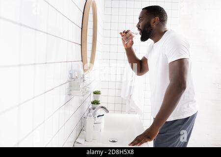 Seitenansicht eines afro-amerikanischen Mannes, der Wasser trinkt und nach innen schaut Spiegel Stockfoto