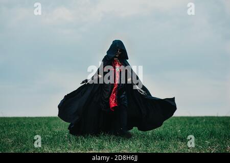 Junge Frau geht über Feld in Halloween Kostüm des Todes mit bemalten Skelett auf ihrem Körper vor Hintergrund Himmel. Halloween-Konzept. Zuckerschädel Stockfoto