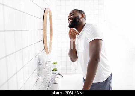 Glücklicher afro-amerikanischer Mann, der in Spiegel schaut und den Bart berührt Badezimmer Stockfoto
