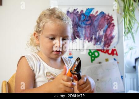 Ein dreijähriges Mädchen schält eine Karotte selbstständig in sich Wohnküche Stockfoto