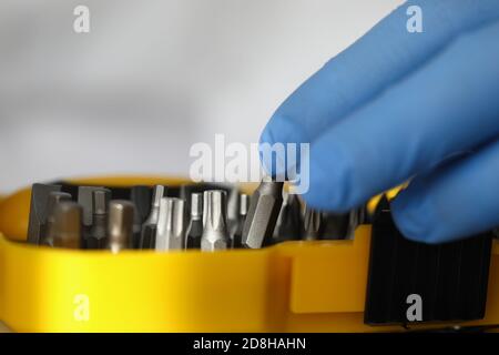 Hand in Gummihandschuh hält Schraubendreher in der Nähe der Box mit Werkzeugen Nahaufnahme Stockfoto