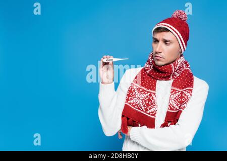 Kranker und verärgerter Mann in Strickmode, der Thermometer isoliert auf zeigt Blau Stockfoto
