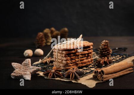 SPECULOOS gestapelt mit Verpackungsband auf einem schwarzen Kühlgitter gewickelt, verziert mit Holzsternen, Zimtstangen und Anis Sterne, im Hintergrund f Stockfoto