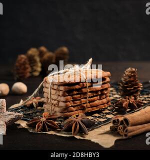 SPECULOOS gestapelt mit Verpackungsband auf einem schwarzen Kühlgitter gewickelt, verziert mit Holzsternen, Zimtstangen und Anis Sterne, im Hintergrund f Stockfoto