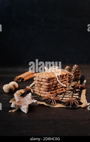 SPECULOOS gestapelt mit Verpackungsband auf einem schwarzen Kühlgitter gewickelt, verziert mit Holzsternen, Zimtstangen und Anis Sterne, im Hintergrund f Stockfoto