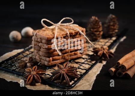 Speculaius gestapelt mit Packband auf einem schwarzen Kühlgitter gewickelt, verziert mit Holzsternen, Zimtstangen und Anis-Sternen, im Hintergrund Stockfoto