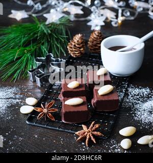 Marzipankuben mit Schokoladenvereisung auf schwarzem Kühlgitter, verziert mit Kiefernzweig, Zimtstangen und Anissternen, Tannenzapfen, daneben eine Schleife Stockfoto